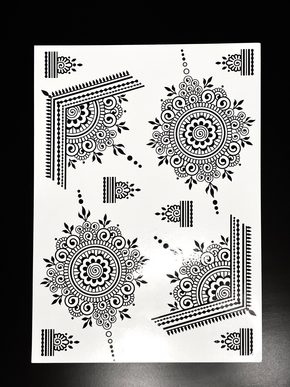 Black mandala henna transfer sheet with intricate circular mehndi designs and decorative corner patterns.