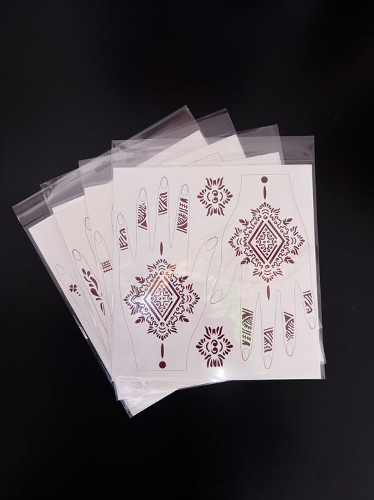 A fanned-out stack of temporary tattoo or henna stencil sheets in clear cellophane sleeves, laid on a dark surface. The top sheet features a sharp geometric design in a rich, dark maroon or burgundy ink, highlighting a large central diamond mandala for the back of the hands, abstract tribal-style finger bands, and two independent accent medallions.