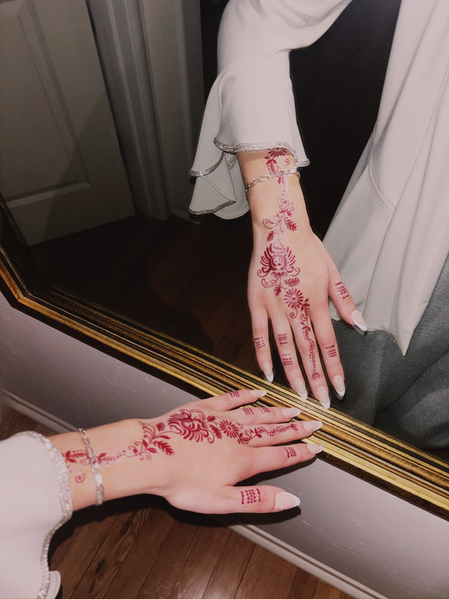 Hands with red floral henna designs in front of a mirror