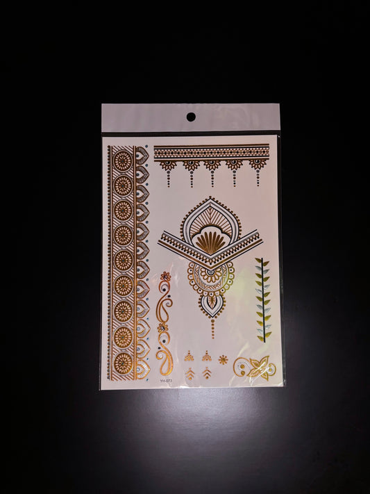 A single metallic gold temporary henna tattoo sheet displayed against a black background on a computer screen. The sheet features intricate decorative designs including floral borders, geometric patterns, paisley-inspired elements, and small accent details in reflective gold and brown tones.