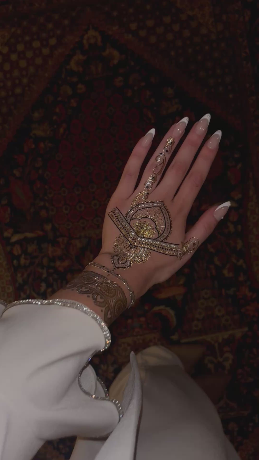 Close-up video of a hand wearing a metallic gold temporary henna tattoo under flash lighting. The intricate design sparkles and reflects light, highlighting detailed floral and geometric patterns with a glossy metallic finish.